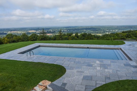 This is a photo of a rectangle inground swimming pool overlooking a town.
