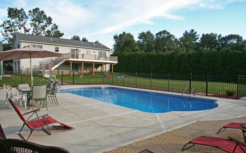 This is a photo of a roman in ground pool in Stuyvesant, NY with custom pavers, black fence and steps.