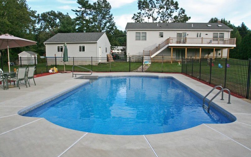 This is a photo of a roman in ground pool in Stuyvesant, NY with custom pavers, black fence and steps.